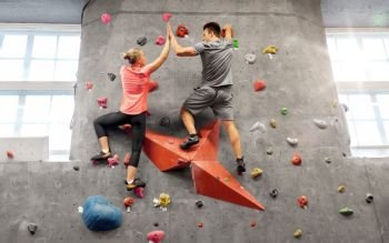 fitness, extreme sport and healthy lifestyle concept - young man and woman bouldering on a rock climbing wall at indoor gym and making high five gesture. man and woman climbing a wall at indoor gym