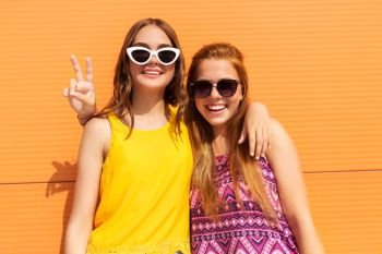 fashion, leisure and people concept - smiling teenage girls in summer clothes hugging and showing peace hand sign outdoors. smiling teenage girls showing peace in summer