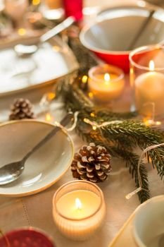 christmas, holidays and decoration concept - table served and decorated for festive dinner with candles, pine cones and fir branch. table served and decorated for christmas dinner