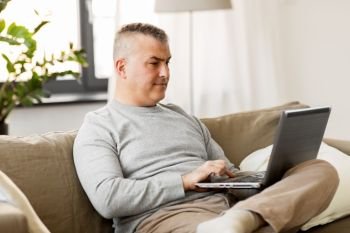 technology, people and lifestyle concept - man with laptop computer sitting on sofa at home. man with laptop computer sitting on sofa at home