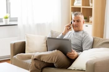 technology, people and lifestyle concept - man with laptop computer sitting on sofa at home and calling on smartphone. man with laptop calling on smartphone at home