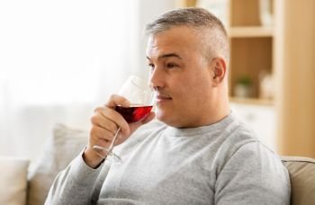 people, alcohol and drinks concept - man drinking red wine from glass at home. man drinking red wine from glass at home
