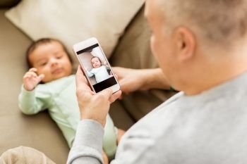 family, fatherhood and people concept - close up of father photographing little baby son by smartphone at home. father photographing baby by smartphone