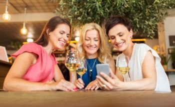 people, technology and lifestyle concept - women with smartphone drinking wine at bar or restaurant. women with smartphone at wine bar or restaurant
