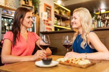 people, celebration and lifestyle concept - happy women drinking red wine and talking at restaurant or bar. happy women drinking red wine at bar or restaurant
