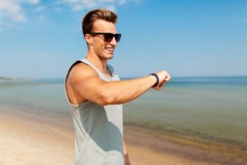 sport, people, technology and healthy lifestyle concept - smiling young man with fitness tracker on summer beach. happy man with fitness tracker on summer beach