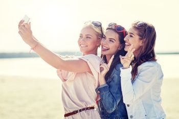 summer vacation, holidays, travel, technology and people concept- group of smiling young women taking selfie with smartphone on beach. group of smiling women taking selfie on beach