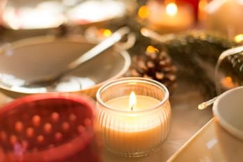 christmas, holidays and decoration concept - candle burning on table served for festive dinner at home. candle burning on christmas table