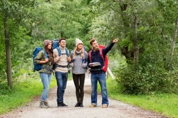 travel, tourism, hiking and people concept - happy friends or travelers with backpacks and map on road in woods. friends or travelers hiking with backpacks and map