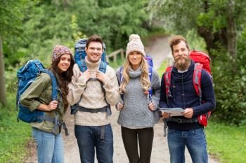 travel, tourism, hiking and people concept - happy friends or travelers with backpacks and map on road in woods. friends or travelers hiking with backpacks and map