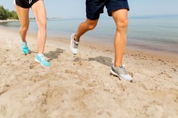 fitness, sport and technology concept - legs of couple of sportsmen in sneakers running along summer beach. legs of sportsmen in sneakers running along beach