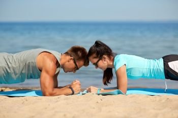 fitness, sport and lifestyle concept - couple doing plank exercise on summer beach. couple doing plank exercise on summer beach