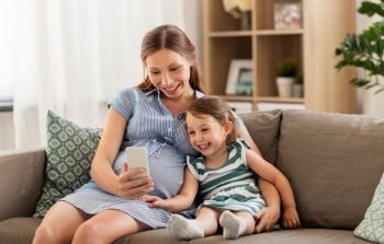 pregnancy, people and family concept - happy pregnant mother and little daughter with smartphone at home. pregnant mother and daughter with smartphone