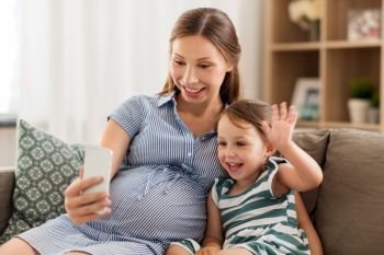 pregnancy, technology and family concept - happy pregnant mother and little daughter having video chat on smartphone at home. pregnant mother and daughter having video chat
