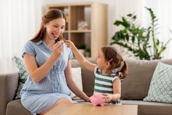 pregnancy, finances and family concept - happy pregnant mother and little daughter putting euro coin into piggy bank at home. pregnant mother and daughter with piggy bank