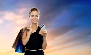 people, luxury and sale concept - beautiful woman with credit card and shopping bags over sky background. woman with credit card and shopping bags
