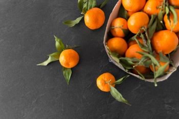 food, healthy eating and vegetarian concept - close up of whole mandarins with leaves on slate table top. close up of mandarins on slate table top