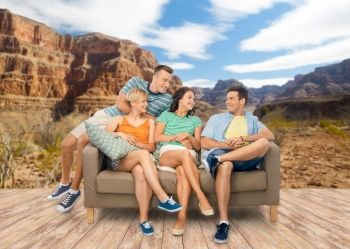 travel, leisure and people concept - group of happy smiling friends sitting on sofa over grand canyon national park background. friends sitting on sofa over grand canyon