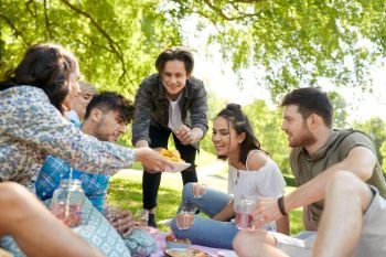 friendship and leisure concept - group of happy friends with non alcoholic drinks and food at picnic in summer park. friends with drinks and food at picnic in park