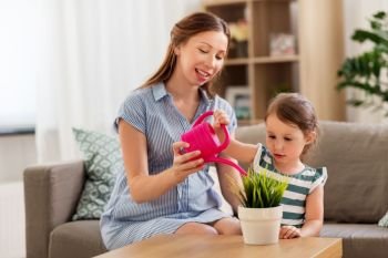 pregnancy, people and family concept - happy pregnant mother teaches her little daughter to take care of home plant with watering can. pregnant mother and daughter watering home plant