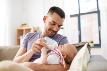 family, parenthood and people concept - father feeding little daughter with baby formula from bottle at home. father feeding baby daughter from bottle at home