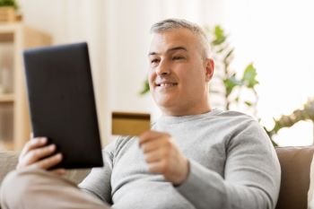 technology, online shopping, people and lifestyle concept - man with tablet pc computer and credit card sitting on sofa at home. man with tablet pc and credit card on sofa at home
