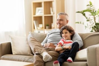 family, fatherhood and people concept - happy father with little son sitting on couch at home and watching tv. happy father with little son at home
