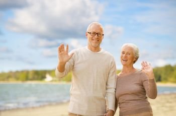 old age, retirement and people concept - happy senior couple waving hands over beach background. happy senior couple waving hands on beach