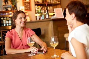 people, celebration and lifestyle concept - happy women drinking wine and talking at bar or restaurant. happy women drinking wine at bar or restaurant