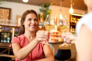 people, celebration and lifestyle concept - happy woman drinking wine and clinking glasses with friend at bar or restaurant. happy women drinking wine at bar or restaurant