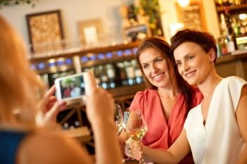 people, technology and lifestyle concept - woman photographing friends drinking wine by smartphone at bar or restaurant. woman picturing friends by smartphone at wine bar