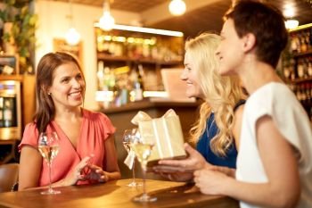 people, celebration and greeting concept - happy women giving birthday present to friend at wine bar or restaurant. women giving present to friend at wine bar