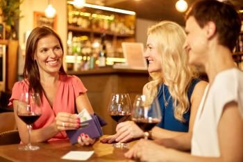 leisure, payment and lifestyle concept - happy women with money in wallet paying bill at restaurant or wine bar. women paying bill at wine bar or restaurant