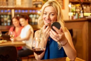 beauty, makeup and lifestyle concept - happy woman with lipstick and mirror at wine bar or restaurant. woman with lipstick applying makeup at wine bar