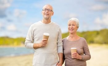 old age, retirement and takeaway concept - happy senior couple with coffee cups over beach background. senior couple with takeaway coffee on beach