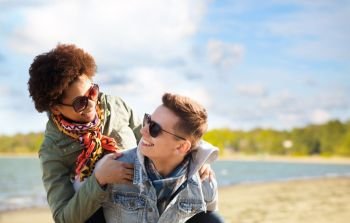 leisure and people concept - happy mixed-race teenage couple in sunglasses having fun over beach background. happy teenage couple in shades having fun on beach
