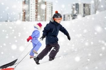 childhood, sledging and season concept - happy little kids with sleds climbing snow hill in winter. kids with sleds climbing snow hill in winter
