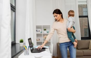 motherhood, multi-tasking, family and technology concept - mother with baby, laptop computer and papers working at home. mother with baby and laptop working at home