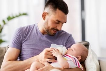 family, parenthood and people concept - father feeding little daughter with baby formula from bottle at home. father feeding baby daughter from bottle at home