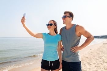fitness, sport and lifestyle concept - happy couple in sports clothes taking selfie by smartphone on beach. couple taking selfie by smartphone on beach
