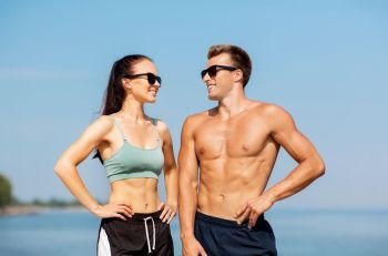 fitness, sport and lifestyle concept - happy couple in sports clothes and sunglasses on beach. happy couple in sports clothes and shades on beach