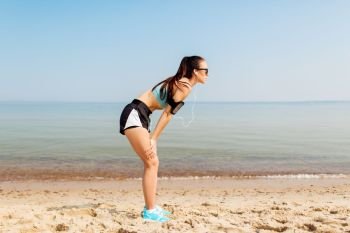 fitness, sport and technology concept - tired female runner with earphones and smartphone in arm band on beach. female runner with earphones and arm band on beach