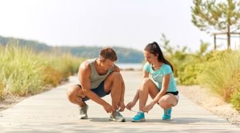 fitness, sport and lifestyle concept - couple of joggers tying sneakers shoelaces outdoors. couple of joggers tying sneakers shoelaces