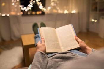 leisure, hygge and christmas concept - close up of young man reading book at home. close up of young man reading book at home