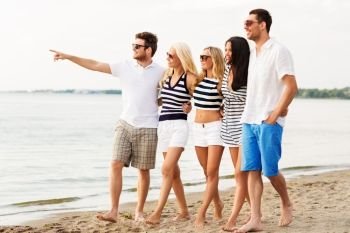 friendship, summer holidays and people concept - group of happy friends in striped clothes walking along sandy beach. friends in striped clothes walking along beach