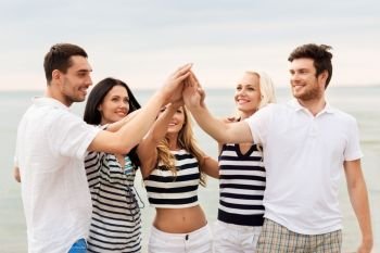 friendship, summer holidays and people concept - group of happy friends in striped clothes making high five on beach. happy friends making high five on beach