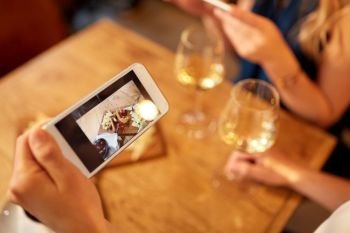 people, technology and lifestyle concept - hand of woman picturing food by smartphone and drinking wine at bar or restaurant. woman picturing food by cell and drinking wine