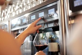 people, alcohol and lifestyle concept - close up of woman with glass pouring red wine from dispenser at bar or restaurant. close up of woman with glass at wine dispenser