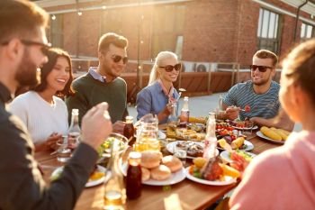 leisure and people concept - happy friends having dinner or barbecue party and eating on rooftop in summer. friends having dinner or bbq party on rooftop