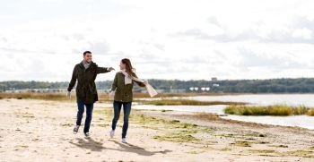 love, relationship and people concept - smiling couple running along autumn beach and holding hands. couple running along autumn beach